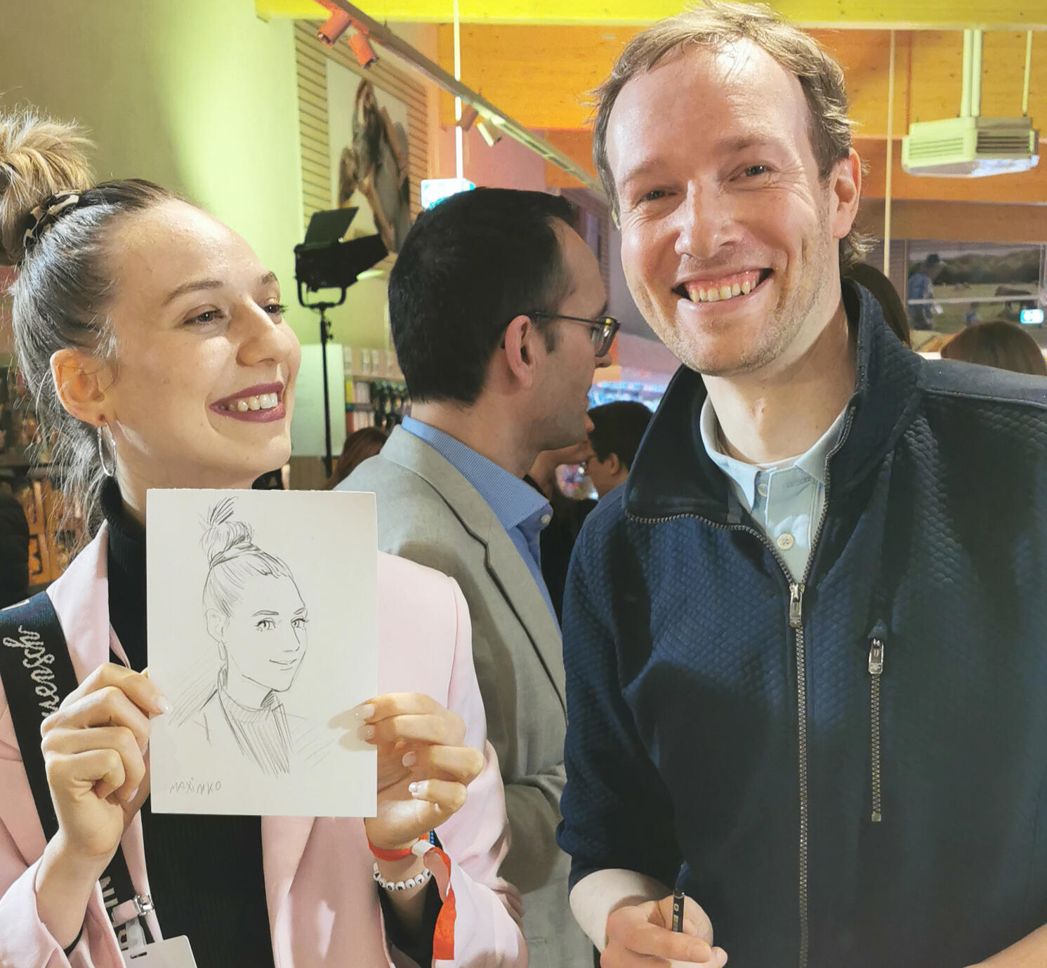 コカ・コーラの企業イベントでのライブ似顔絵。完成したA5サイズの似顔絵を手に、ゲストと笑顔のポートレート。マキシム・シモネンコの実演。